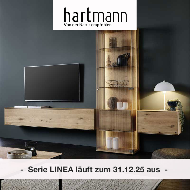 Hartmann LINEA - Massivholzmöbel aus Kerneiche Natur kombiniert mit satiniertem Glas. Möbelprogramm läuft zum 31.12.25 aus!Ambientebild zeigt zwei Hängelowboards, dazwischen eine Standvitrine aus satiniertem Glas mit integriertem Holzschrank.
