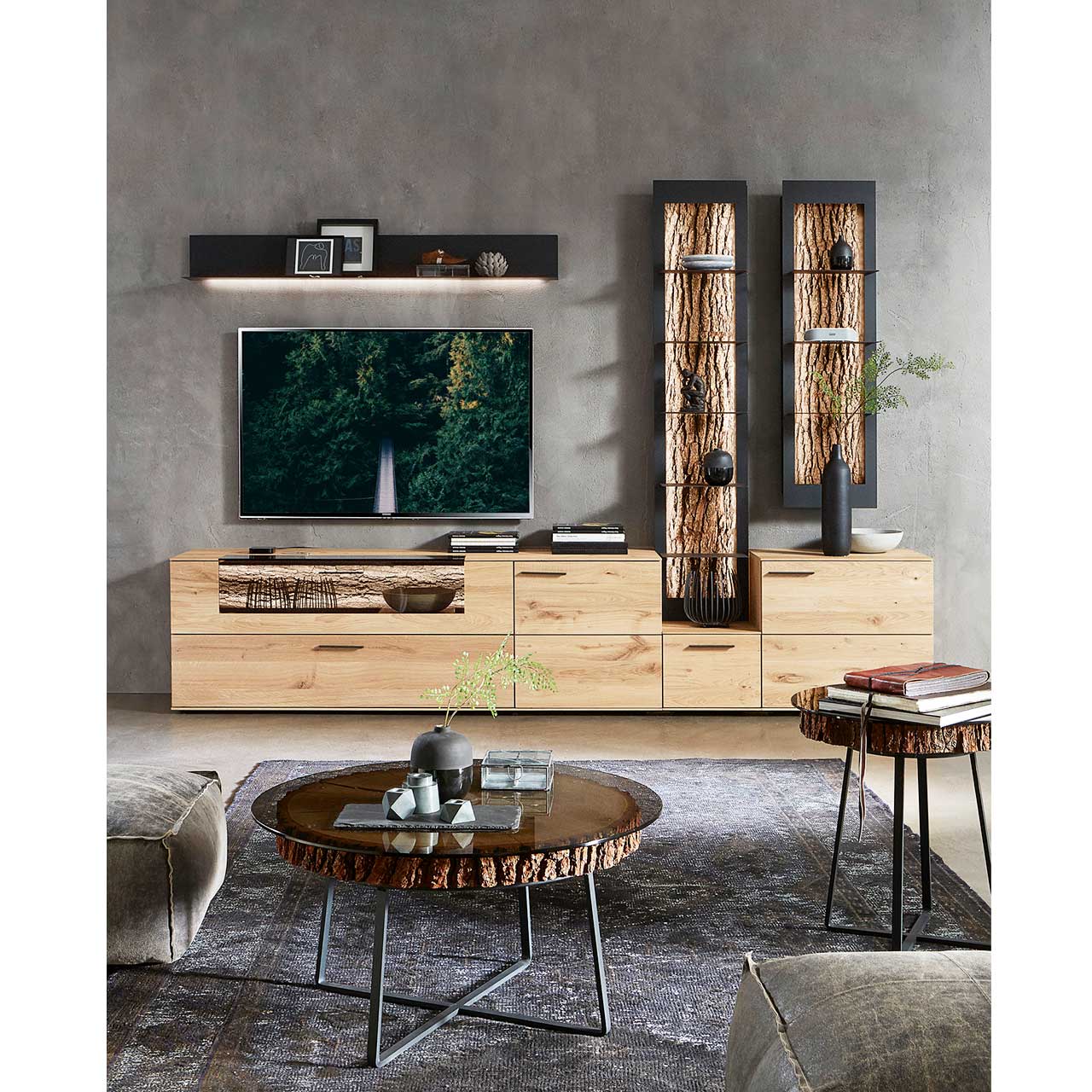 Wohnzimmer mit moderner Massivholz Wohnwand: Lowboard, Wandpaneel und zwei Wandregale. Im Vordergrund ein kleiner und ein großer Beistelltisch mit runder Glasplatte auf echter Baumscheibe und filigranem Metallgestell in Anthrazit.