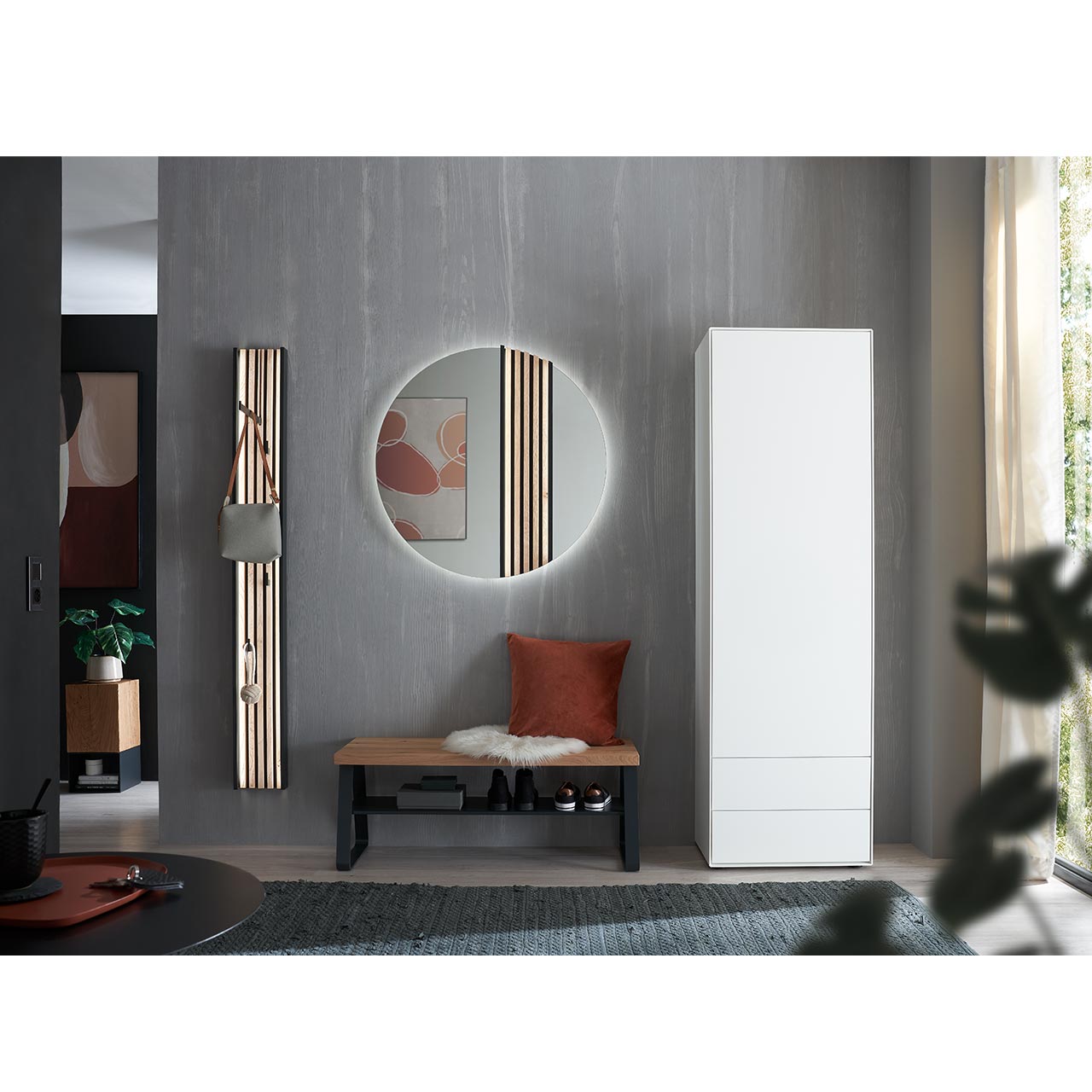 Moderner Flur mit rundem Spiegel mit Lamellen-Akzent, Sitzbank aus Kerneiche Natur mit Metallablageboden, schmales Wandpaneel mit Lamellen-Rückwand, Kleiderstange und Haken und einem Hochschrank in massiver Kerneiche weiß Lackiert mit Schubkästen.