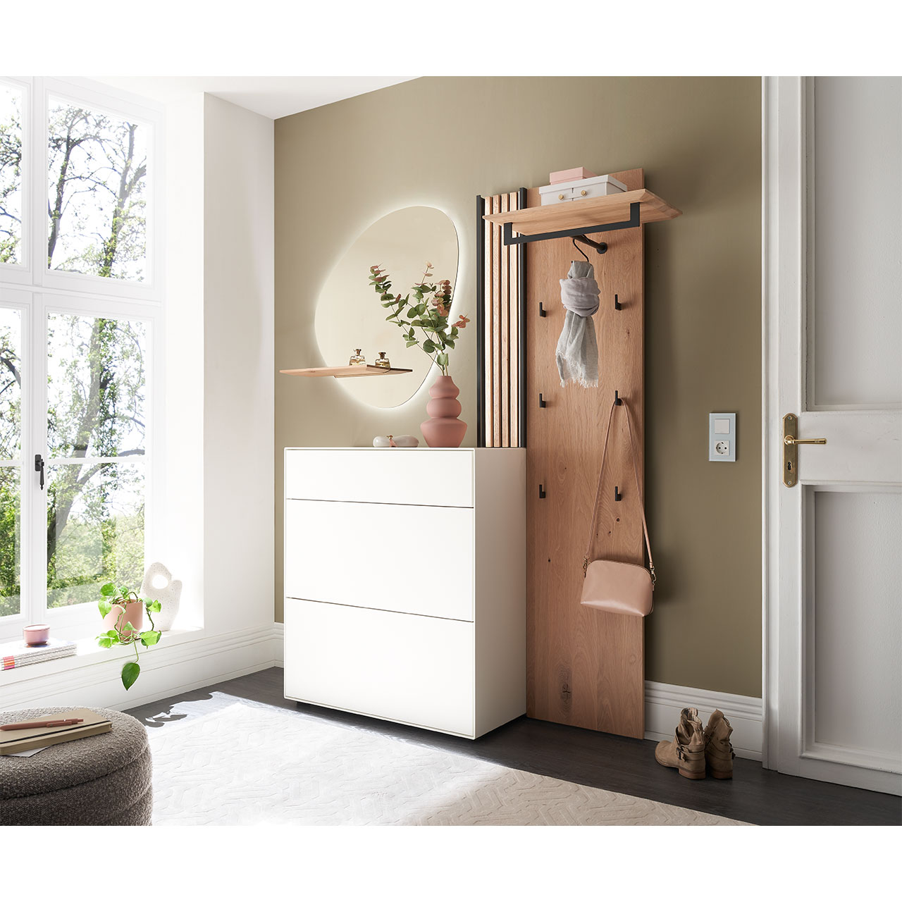 Flur mit modernen Garderobenmöbeln aus Kernbirke und Kerneiche Natur: Wandpaneel aus Holz mit Kleiderstange, Haken und Lamellen-Akzent. Ein Stauraumschrank mit Schubkasten und Klappen in Lack weiß, ein ovaler Spiegel mit Ablage.