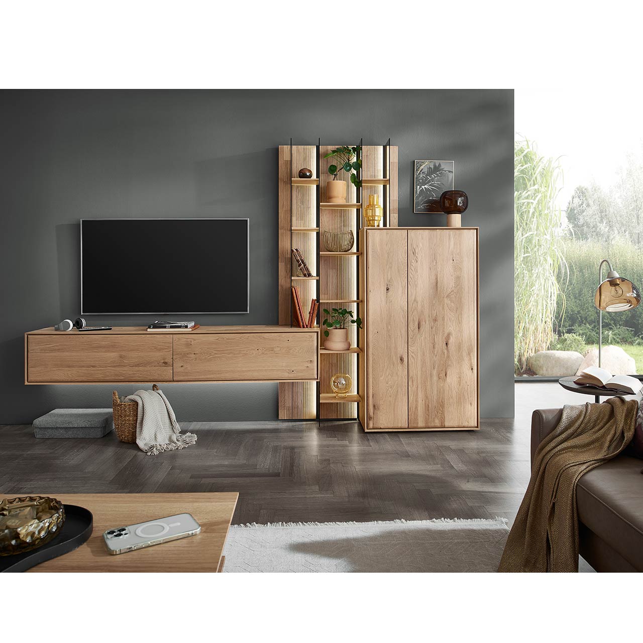Modernes Wohnzimmer mit dreiteiliger Massivholzwohnwand bestehend aus einem Highboard, einem hohen Wandregal mit Holzböden, beleuchteten Glasseiten und geschroppter Rückwand und einem darin integriertem Hängelowboard. Davor passender Couchtisch.