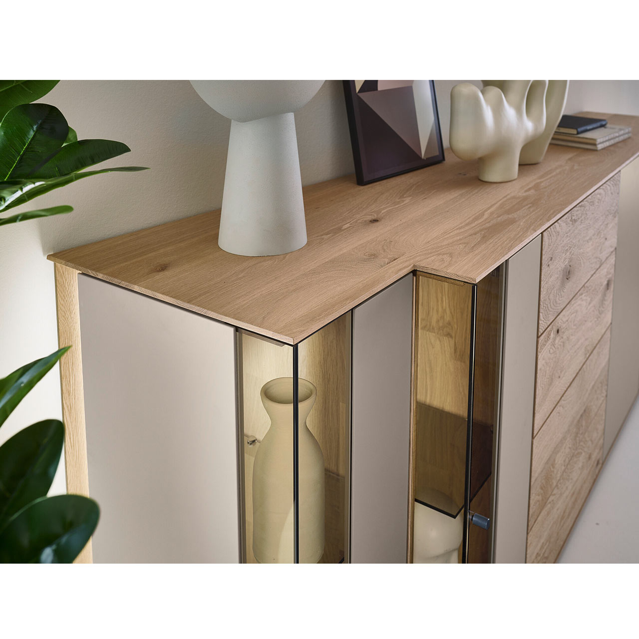 Detailansicht des modernen Sideboards SVEA Nr. 4202 aus massiver Kerneiche Natur und Lack Sand mit asymmetrischer Front aus Glas- und Holzelementen sowie dekorierter Ablagefläche.