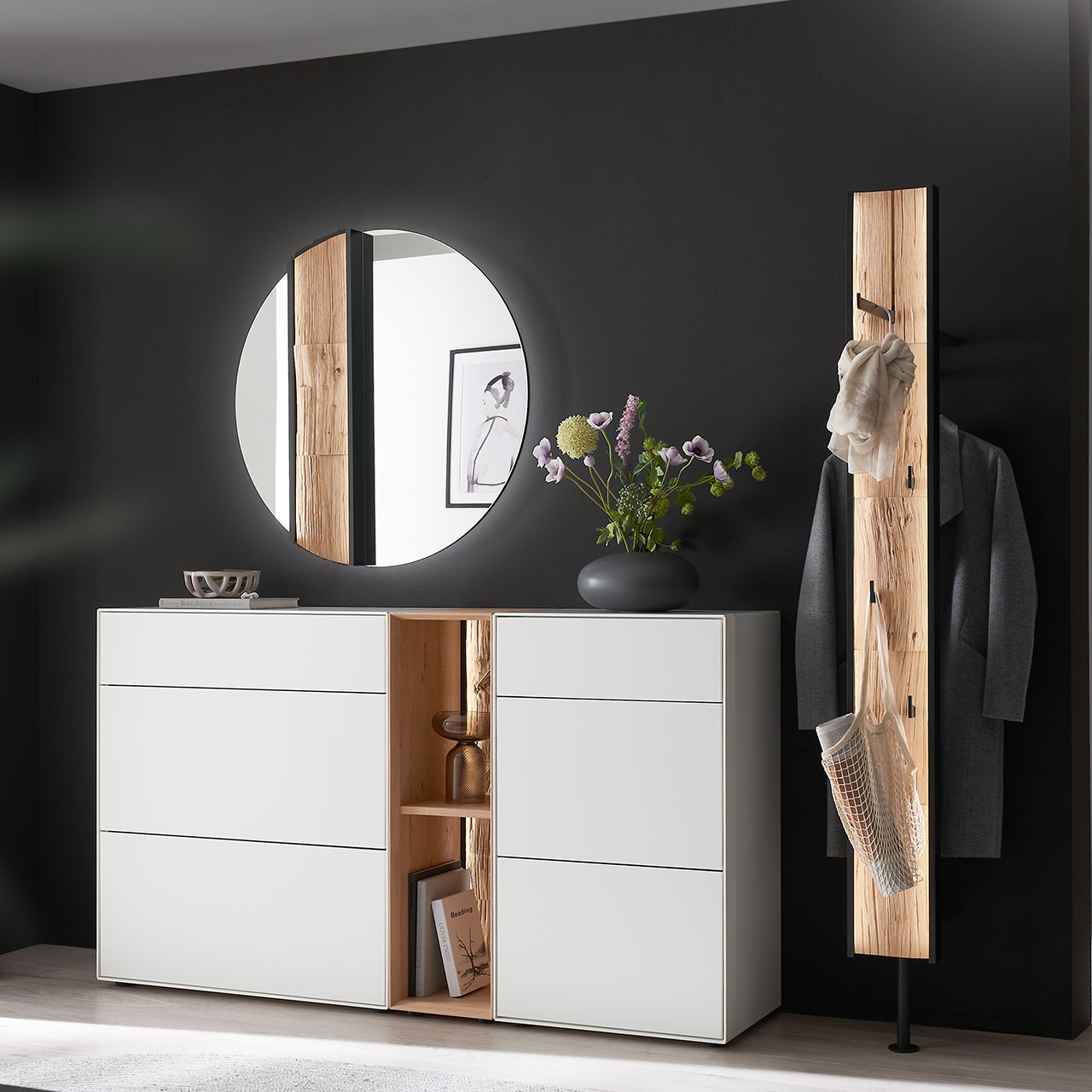 Moderne fünfteilige Garderobe aus massiver Kernbirke und Kerneiche Natur: Regalelement mit Spaltholz-Rückwand zwischen zwei weiß lackierten Stauraumschränken, dazu ein Garderobenpaneel und ein runder Spiegel mit Spaltholz-Akzent.