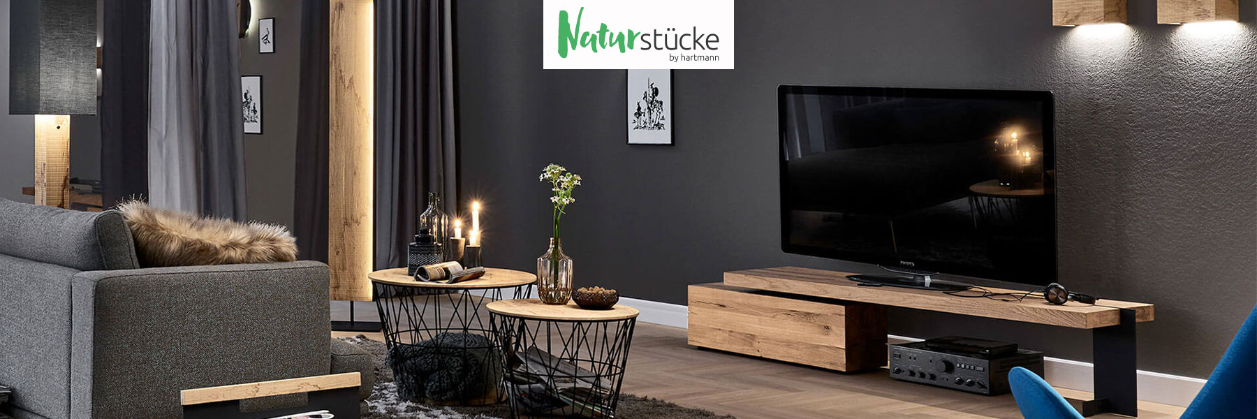 Hartmann Möbel - Möbelserie NATURSTÜCKE - Kerneiche, Birke, Esche Hartmann NATURSTÜCKE - extravagante Wohnaccessoires aus massiver Birke, Esche oder Kerneiche kombiniert mit Glas und Metall. Ambientebild zeigt verschiedene Stehlampen, Zeitungsständer, Wandleuchten, Beistelltische aus hochwertigem Holz.