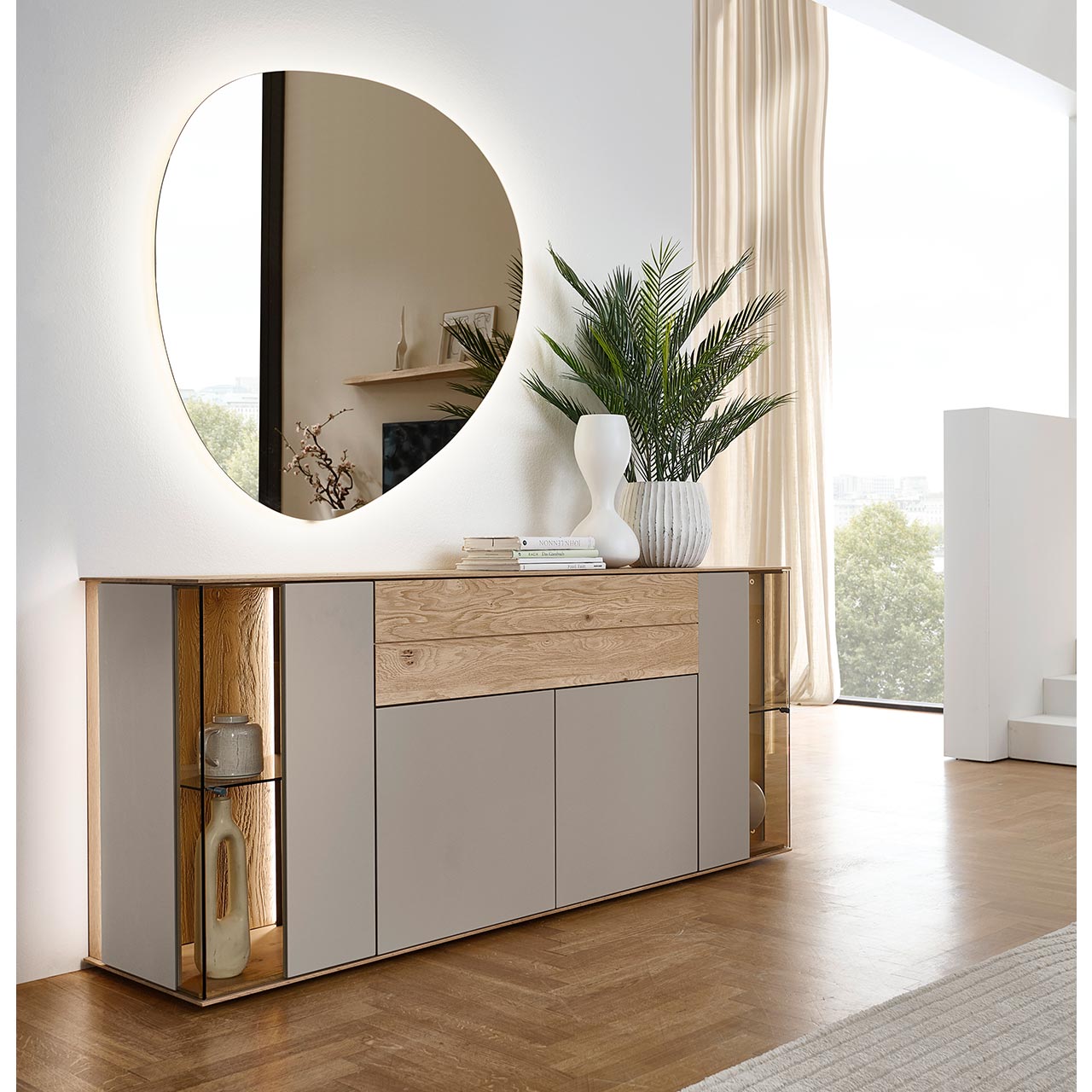 Modernes Sideboard aus massiver Kerneiche Natur mit Lackfronten in Sand und Riffholz. Mit zwei Lacktüren unten, einem langen Schubkasten mit Riffholzfront oben und je einer Glas-Lacktür rechts und links mit beleuchteter Riffholzrückwand - in Frontansicht.