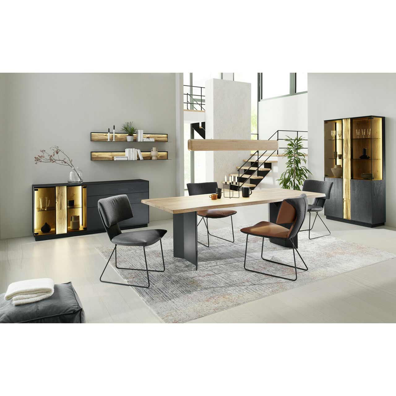 Modern eingerichtetes Esszimmer mit Esstisch aus massiver Kerneiche und anthrazit gebeizten Beinen, dazu vier passende Stühle. Links ein dunkles Sideboard mit Glastüren, rechts ein passendes beleuchtetes Highboard.