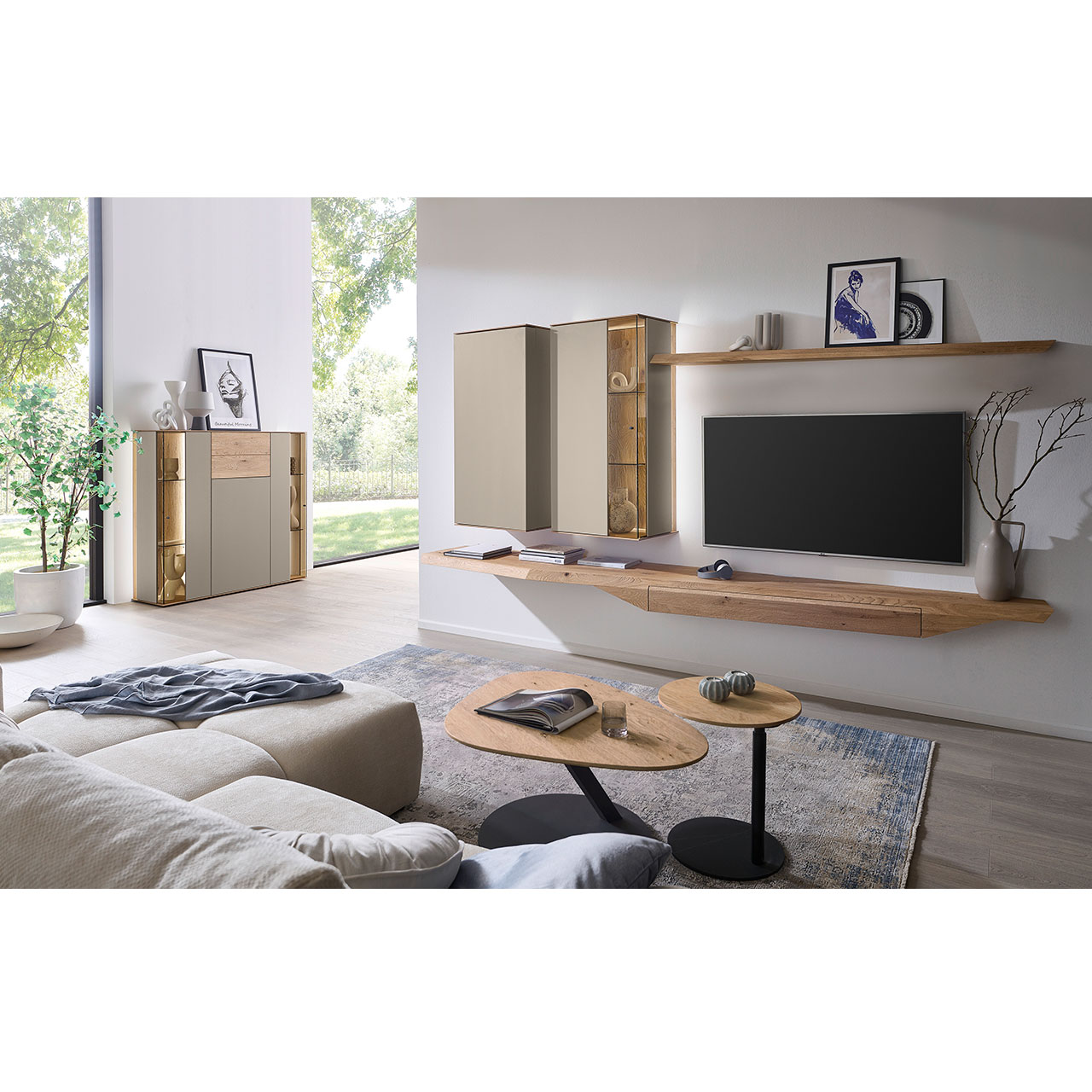 Wohnzimmer mit moderner Massivholzwohnwand bestehend aus Hängelowboard mit Schubkasten, Hängevitrine, Hängeschrank sowie Wandboard - im asymmetrischen Design. Links passendes Sideboard mit Glastüren, davor zwei Beistelltische aus Holz.