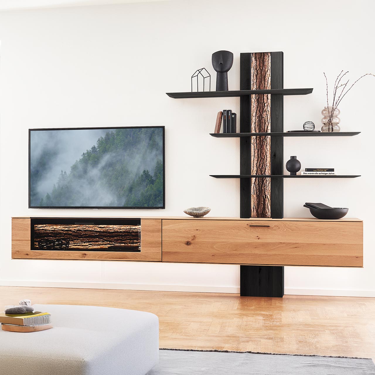 Hartmann RUNA 8410 - Wohnwand Nr. V44 - dreiteilig - Kerneiche Natur und Baumrinde Moderne dreiteilige Wohnwand bestehend aus zwei Hängelowboards aus massiver Kerneiche Natur, eines mit beleuchtetem Glasausschnitt und Rinden-Akzent, und einem Wandpaneel mit sichtbarer Rinden-Rückwand und drei langen, beleuchteten Holzböden.