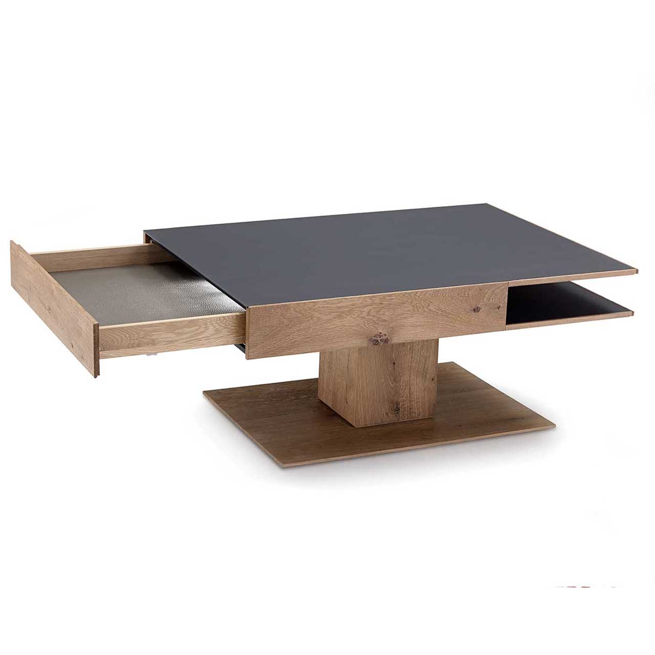Moderner, rechteckiger Couchtisch aus massiver Kerneiche Umato. Dicke Tischplatte in Mattglas Anthrazit mit integriertem, geöffnetem Schubkasten und seitlichem Ablagefach, auf massiver, rechteckiger Holzsäule und Bodenplatte stehend.
