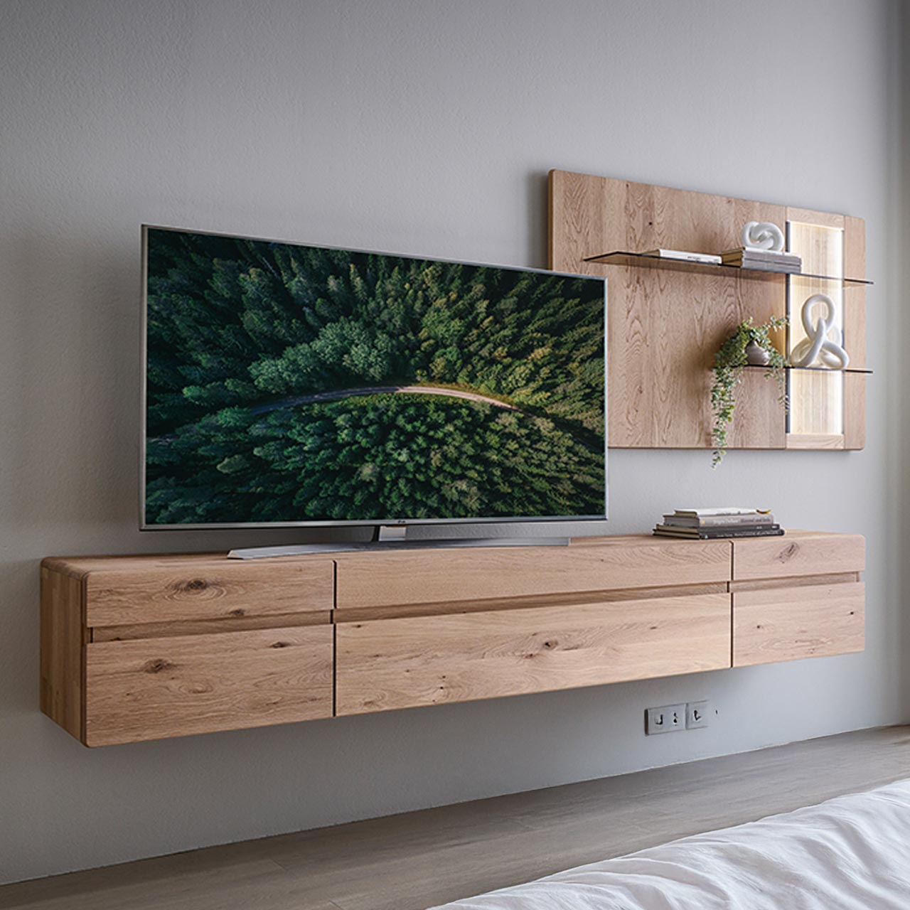 Moderne zweiteilige Wohnwand aus massiver Kerneiche Natur bestehend aus einem langen Hängelowboard mit Türen und Klappe sowie einem Wandpaneel mit beleuchteten Glasböden sowie geschroppter Rückwand.