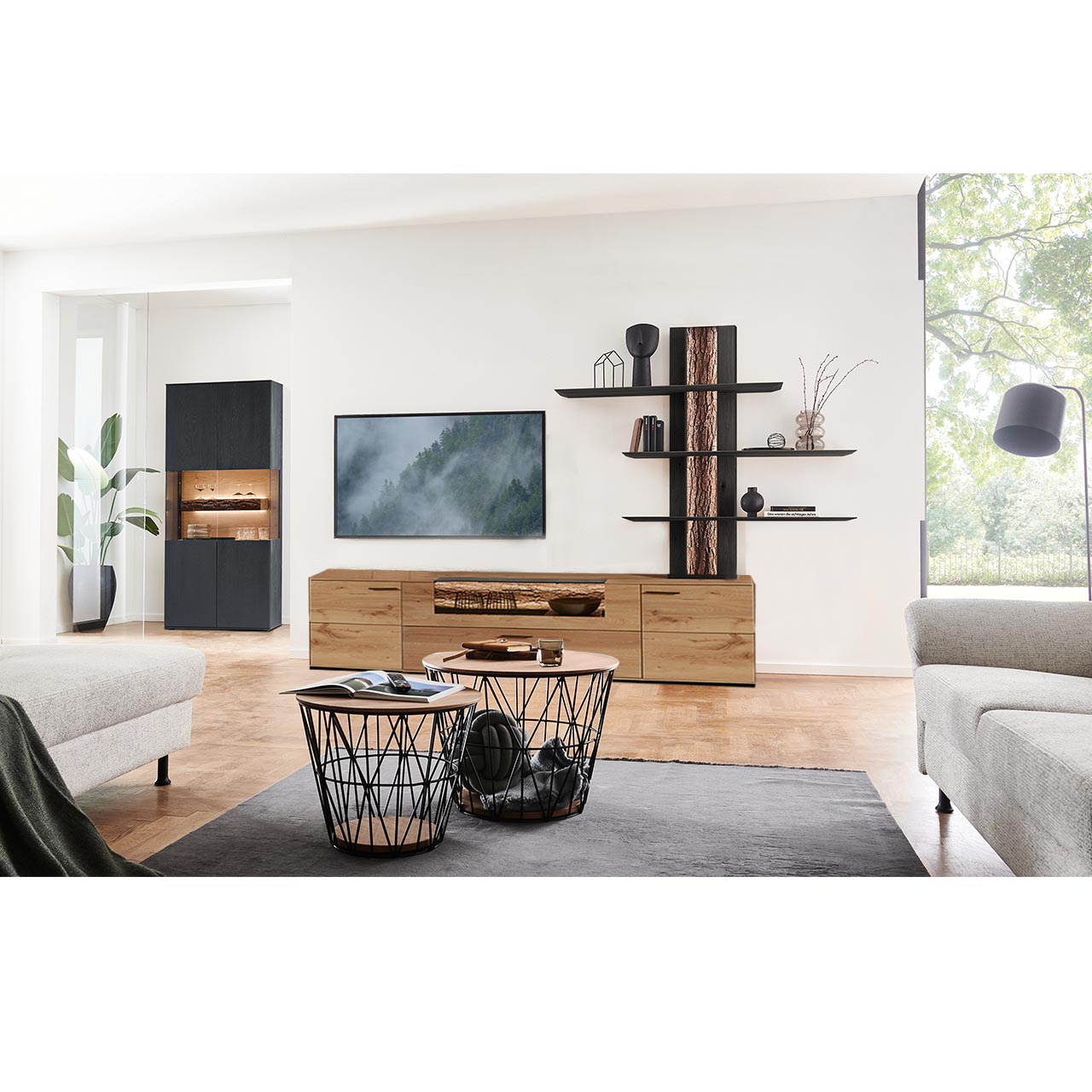 Wohnzimmer mit Wohnwand bestehend aus einem Lowboard mit beleuchtetem Glasausschnitt und einem Anstellelement aus massiver Kerneiche Natur sowie einem Wandpaneel mit drei Ablageböden und sichtbarer Rinden-Rückwand. Links passende Standvitrine.