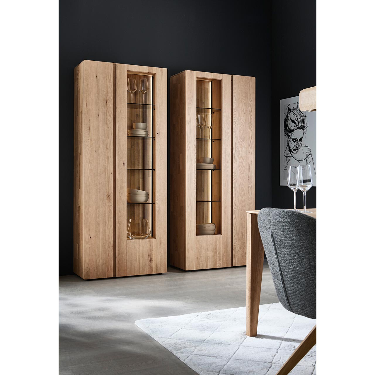 Zwei moderne Standvitrinen aus massivem Eichenholz mit je zwei geschlossen Holz - und Glas/Holztüren. Hinter der Glasfront sichtbar die edel geschoppte Rückwand und je vier beleuchtete Glaseinlegeböden - im Esszimmer stehend.