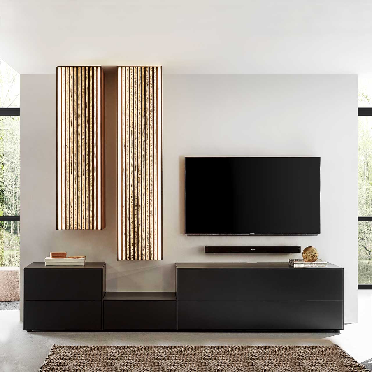 Hartmann SELINO - Wohnwand 8560 Nr. V24 Wohnzimmer mit Fernseher und moderner fünfteiliger Wohnwand aus massivem Holz: Drei schlichte unterschiedlich hohe Lowboards anthrazit lackiert und zwei unterschiedlich hohe Hängeschränke mit hellen Holzlamellen – vor heller Wand.