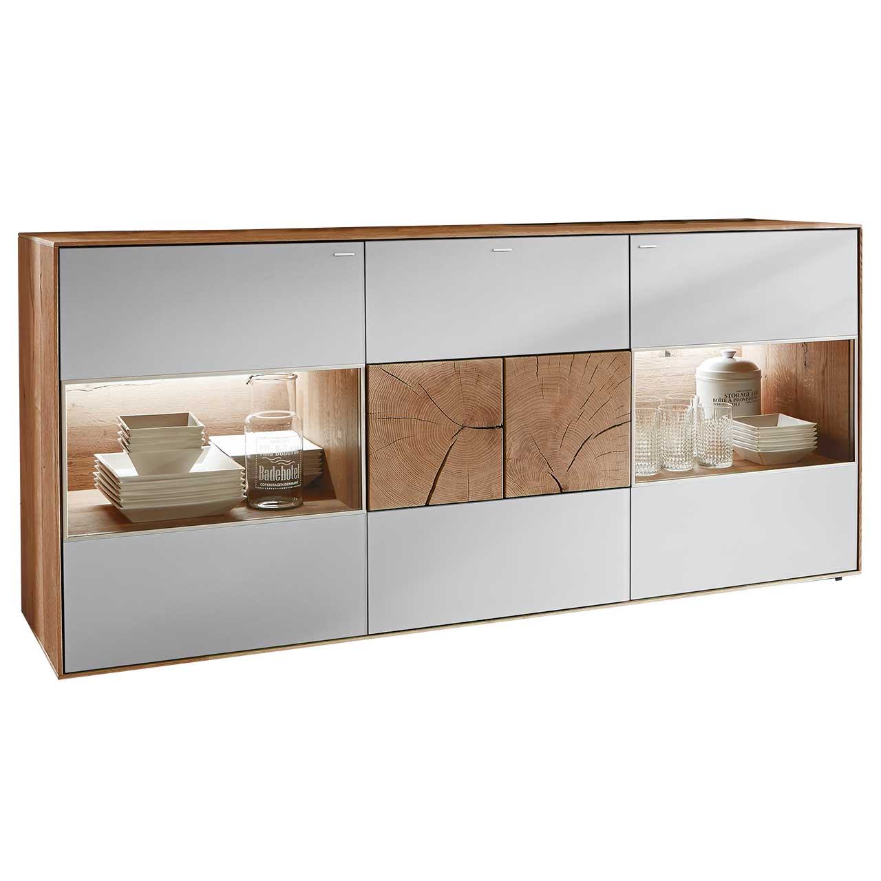 Hartmann CAYA - Sideboard mit Glastüren 7170-4178W Modernes Sideboard aus massiver Kerneiche Umato mit weißfarbenen Mattglasfronten. Rechts und links mit beleuchtetem Glasausschnitt, mittig mit zwei dekorativen, rechteckigen Hirnholzscheiben.