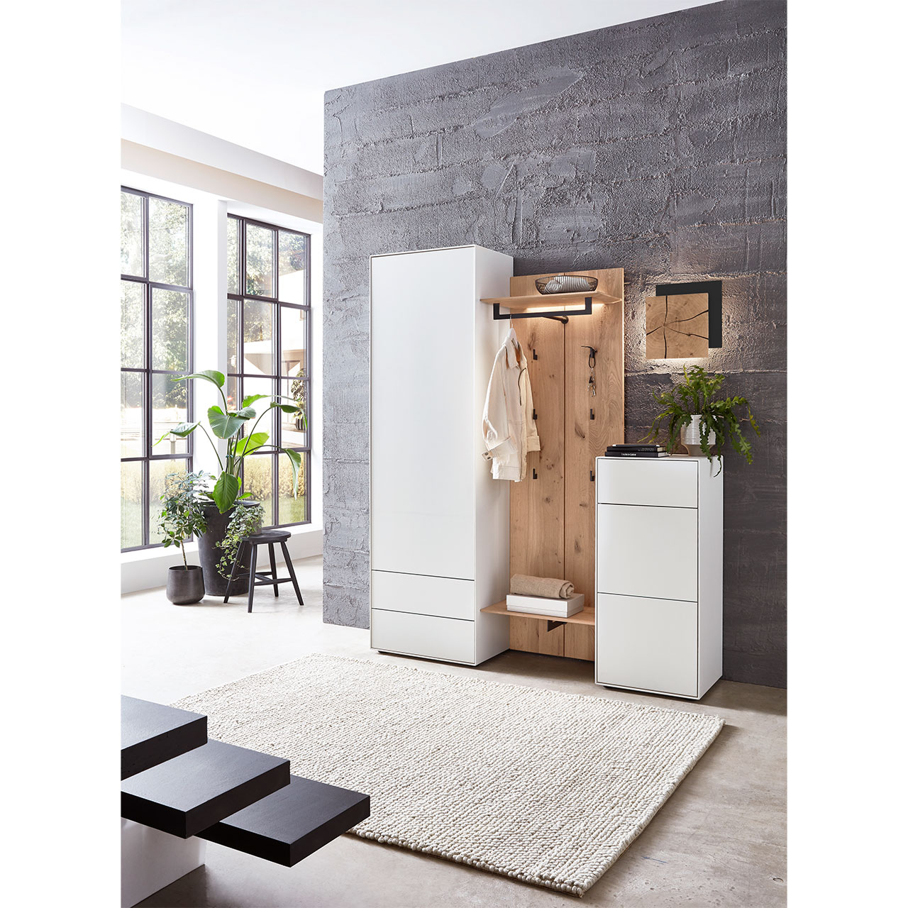 Flur mit modernen Garderobenmöbeln aus massiver Kernbirke und Kerneiche Natur: Ein Hochschrank und Stauraumschrank in Lack weiß, dazwischen eine Wandgarderobe mit Haken und Ablageböden in Holz und eine Wandleuchte mit Hirnholz.