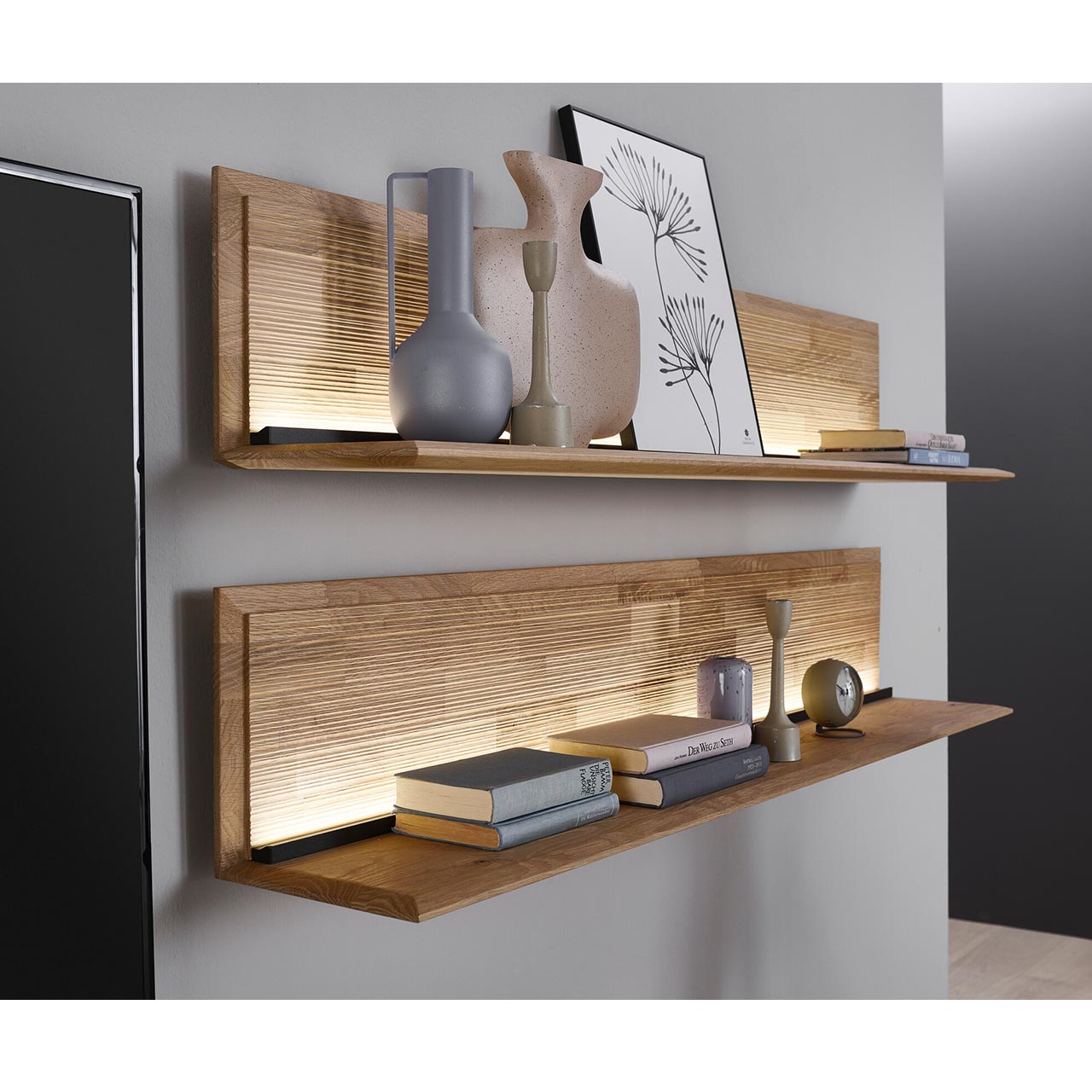 Zwei moderne Wandpaneele aus massiver Kerneiche Natur mit geschroppter Rückwand und einem beleuchtetem Holzablageboden. Die Paneele sind untereinander an der Wand befestigt und mit Vasen und Büchern dekoriert.
