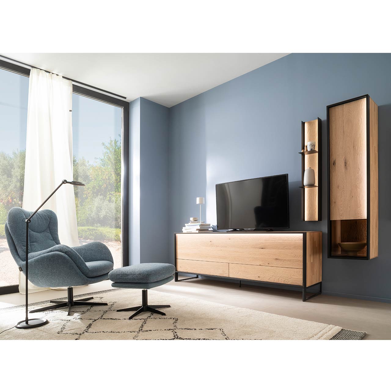 Modernes Wohnzimmer mit TV und dreiteiliger Wohnwand aus massiver sandgestrahlter Kerneiche Natur, Möbelstücke eingefasst in Metall anthrazit: Schlichtes Lowboard auf Metallkufen, Hängeschrank mit beleuchtetem Glasausschnitt, Regal mit drei Metallablagen.