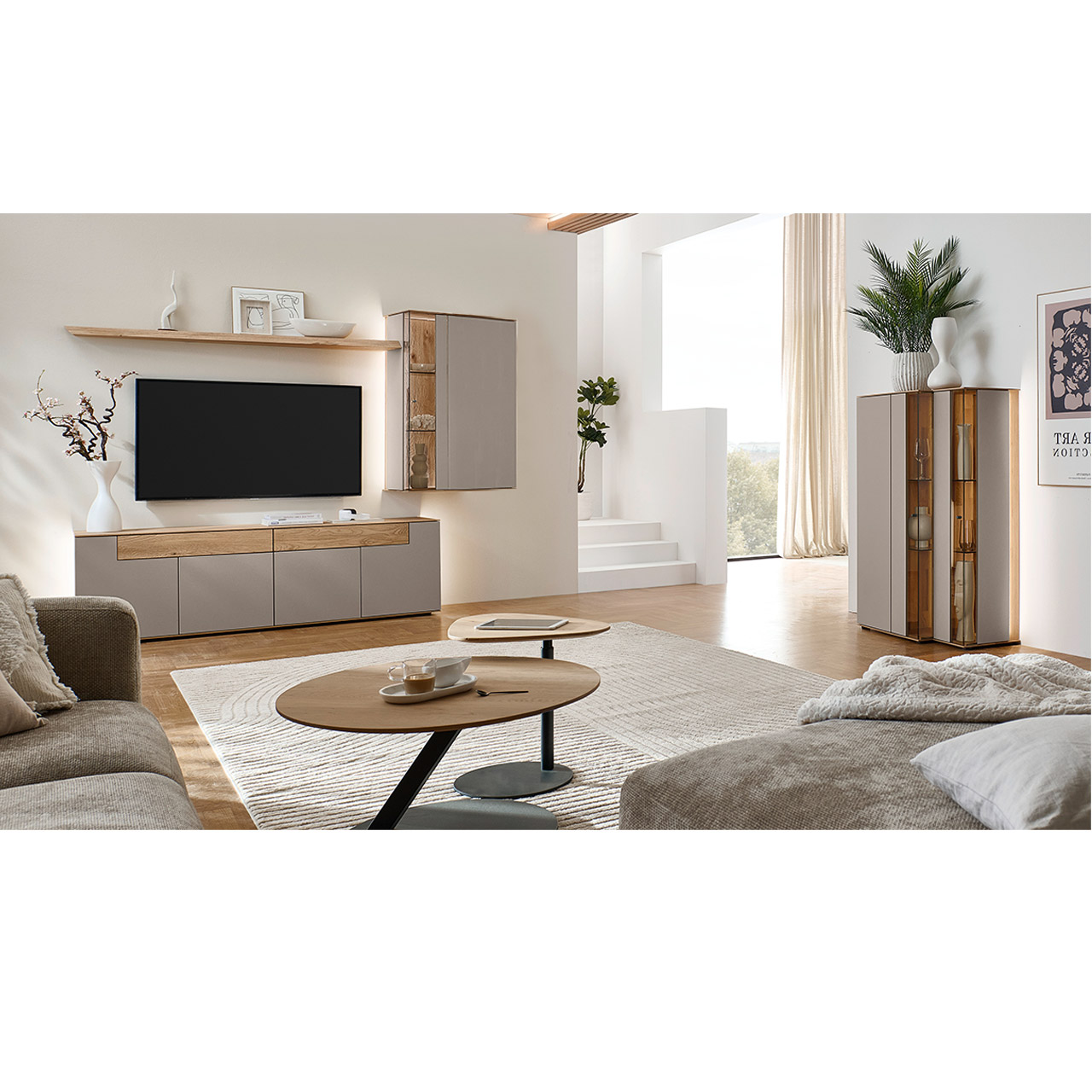 Wohnzimmer mit moderner Massivholzwohnwand bestehend aus einem Lowboard mit Schubkästen, einer Hängevitrine sowie einem Wandboard - im asymmetrischen Design. Rechts passendes Highboard mit Glastüren, davor Holz-Couchtisch.