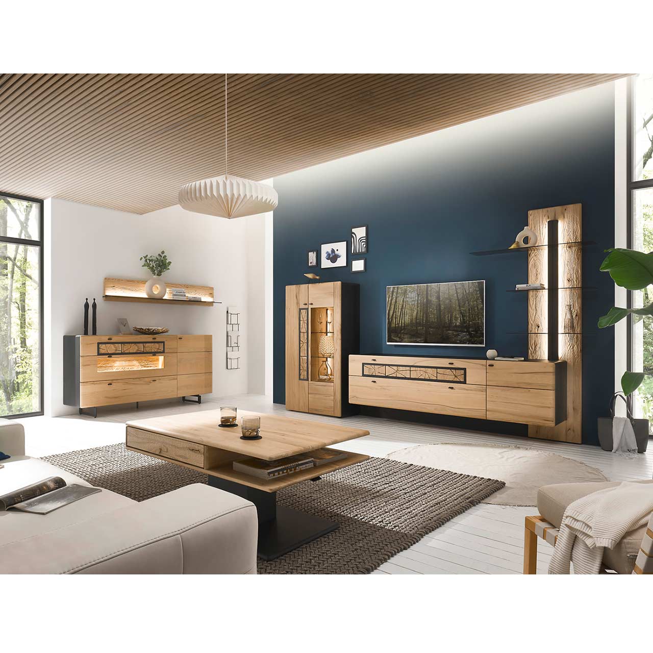 Wohnzimmer mit Wohnwand aus Kernbuche vor einer dunkelblauen Wand bestehend aus Highboard, Lowboard und Paneel mit 3 untereinander angeordneten Glasböden. Rechts das passende Sideboard darüber ein Regal. Im Vordergrund der dazugehörige Couchtisch.