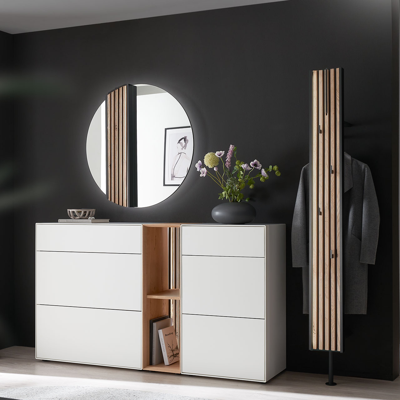 Moderne fünfteilige Garderobe aus massiver Kernbirke und Kerneiche Natur: Regalelement mit Lamellen-Rückwand zwischen zwei weiß lackierten Stauraumschränken, dazu ein Garderobenpaneel und ein runder Spiegel mit Lamellen-Akzent.