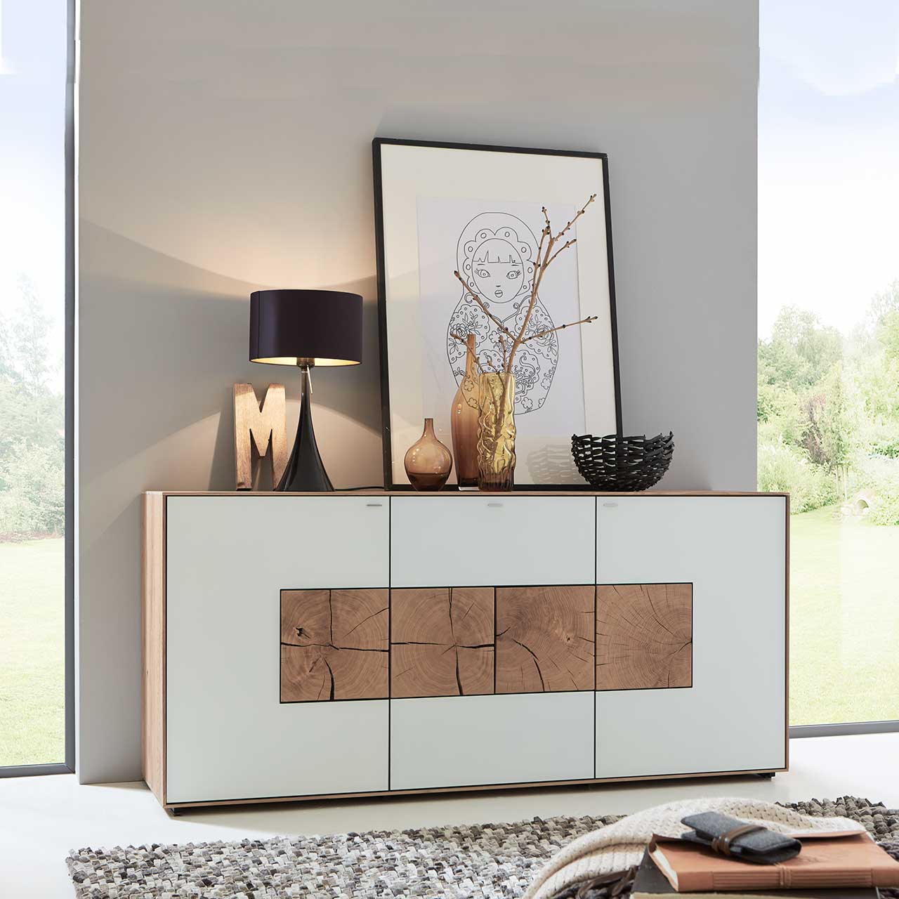 Sideboard Caya aus massiver Kerneiche Umato mit Mattglasfronten weiß und vier dekorativen, rechteckigen Hirnholzscheiben - vor hellgrauer Wand.