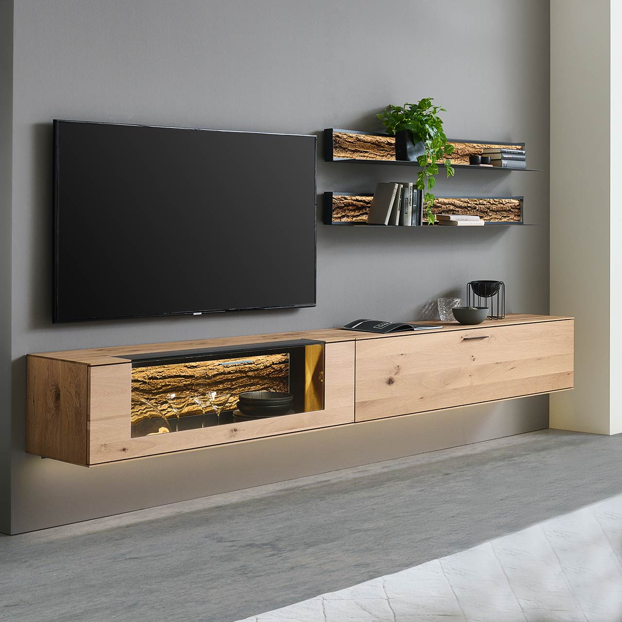Hartmann RUNA 8410 - Wohnwand Nr. V60 - vierteilig - Kerneiche Natur gebürstet und Baumrinde Moderne vierteilige Wohnwand bestehend aus zwei Hängelowboards aus massiver Kerneiche Natur, eines mit beleuchtetem Glasausschnitt und Rinden-Akzent, dazu zwei moderne Metall-Wandregale mit sichtbarer Baumrinde.
