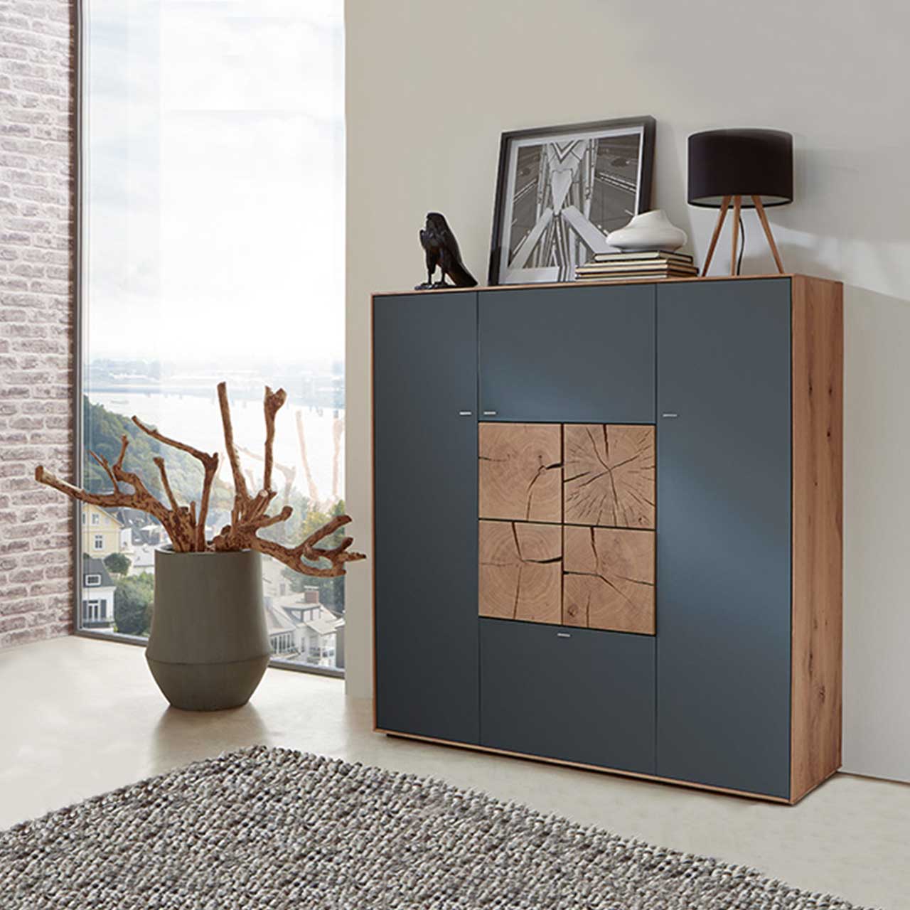 Milieubild Hartmann CAYA - Highboard 7170-7133A Modernes Highboard aus massiver Kerneiche Umato mit Mattglas anthrazit Fronten und vier in der Mitte zum Quadrat zusammengesetzten, dekorativen Hirnholzscheiben in heller Kerneiche Umato - in einem modernen Flur stehend.