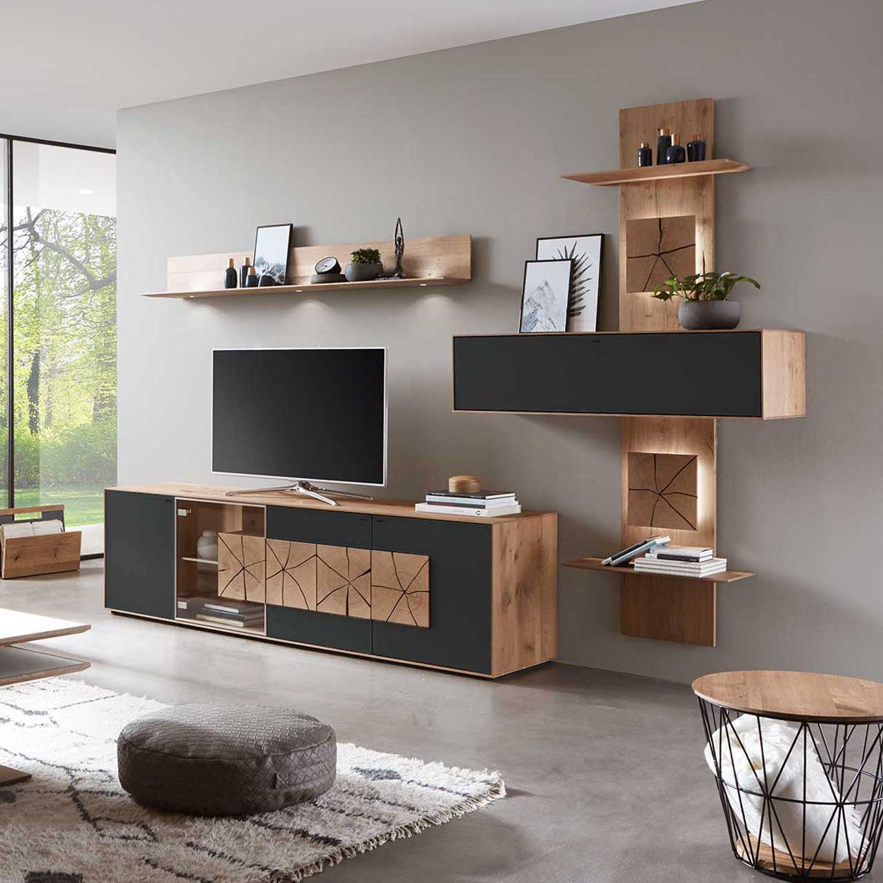 Wohnzimmer mit TV und moderner Wohnwand aus massiver Kerneiche Umato mit Mattglas anthrazit Fronten: Lowboard mit Glastür und Hirnholzscheiben, länglicher Hängeschrank eingefasst in beleuchtetes Wandpaneel mit Ablageböden, daneben Hängeregal aus Holz. 