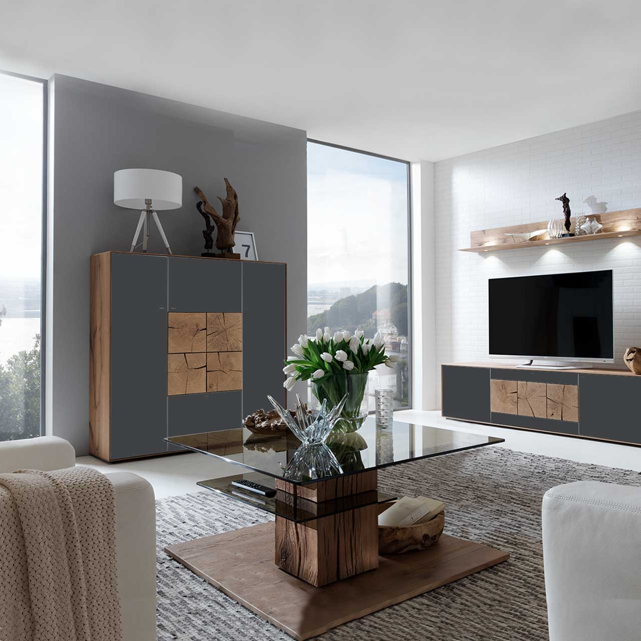 Modernes Highboard aus massiver Kerneiche Umato mit Mattglas anthrazit Fronten und vier dekorativen, rechteckigen Hirnholzscheiben in heller Kerneiche Umato mittig platziert - in einem Wohnzimmer stehend, davor passender Glas-Couchtisch.