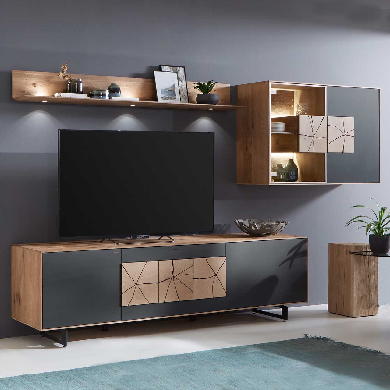 Hartmann CAYA - Wohnkombination 7170 Nr. 62A Moderne dreiteilige Massivholz Wohnwand aus Kerneiche Umato mit Mattglas anthrazit Fronten: Lowboard mit dekorativem Hirnholz auf Metallkufen, Wandregal aus Holz, Hängevitrine mit beleuchtetem Glasausschnitt und Hirnholz.