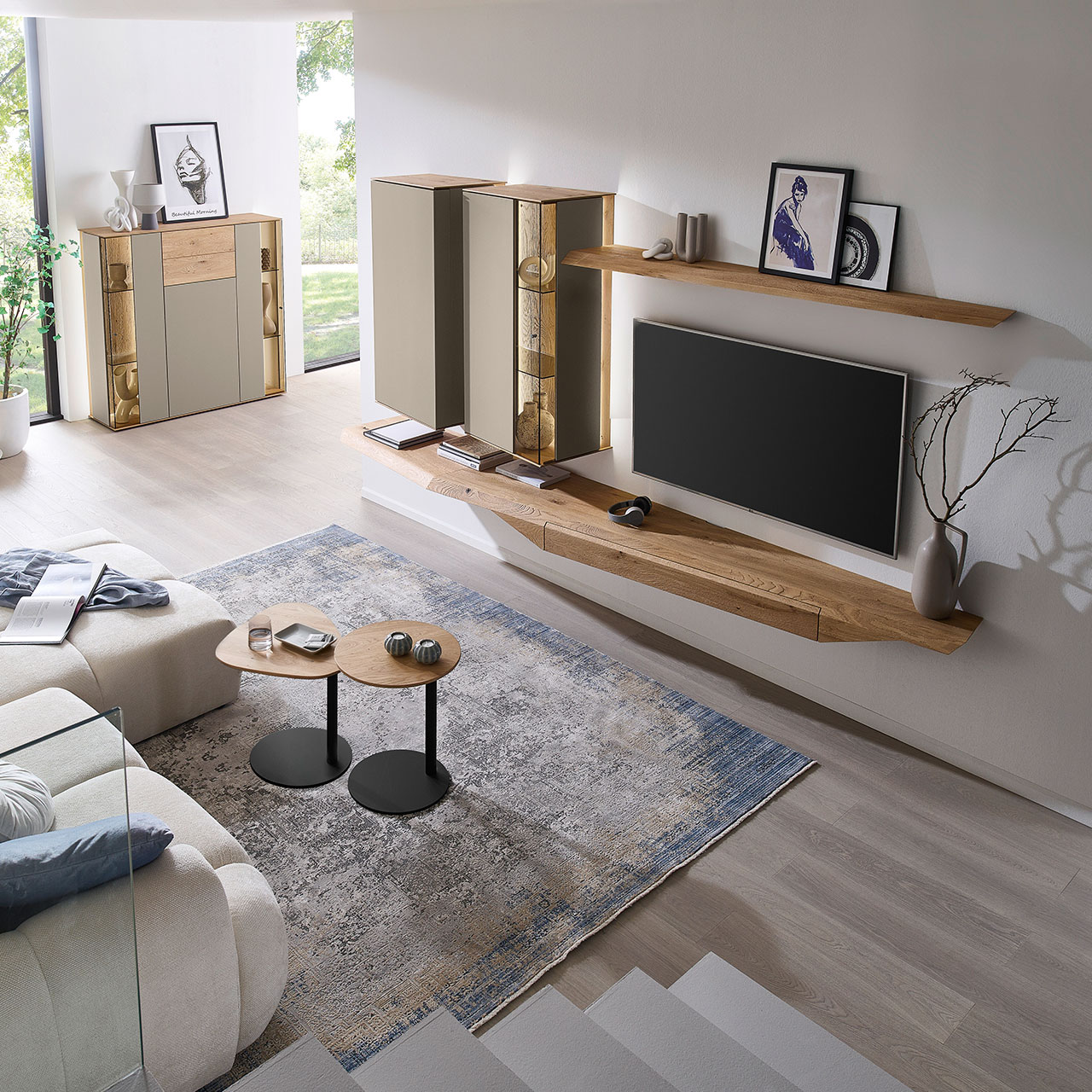 Wohnzimmer mit moderner Massivholzwohnwand bestehend aus Hängelowboard, Hängevitrine, Hängeschrank sowie Wandboard - im asymmetrischen Design. Links passendes Highboard mit Glastüren, davor zwei Beistelltische aus Holz - Ansicht von oben.