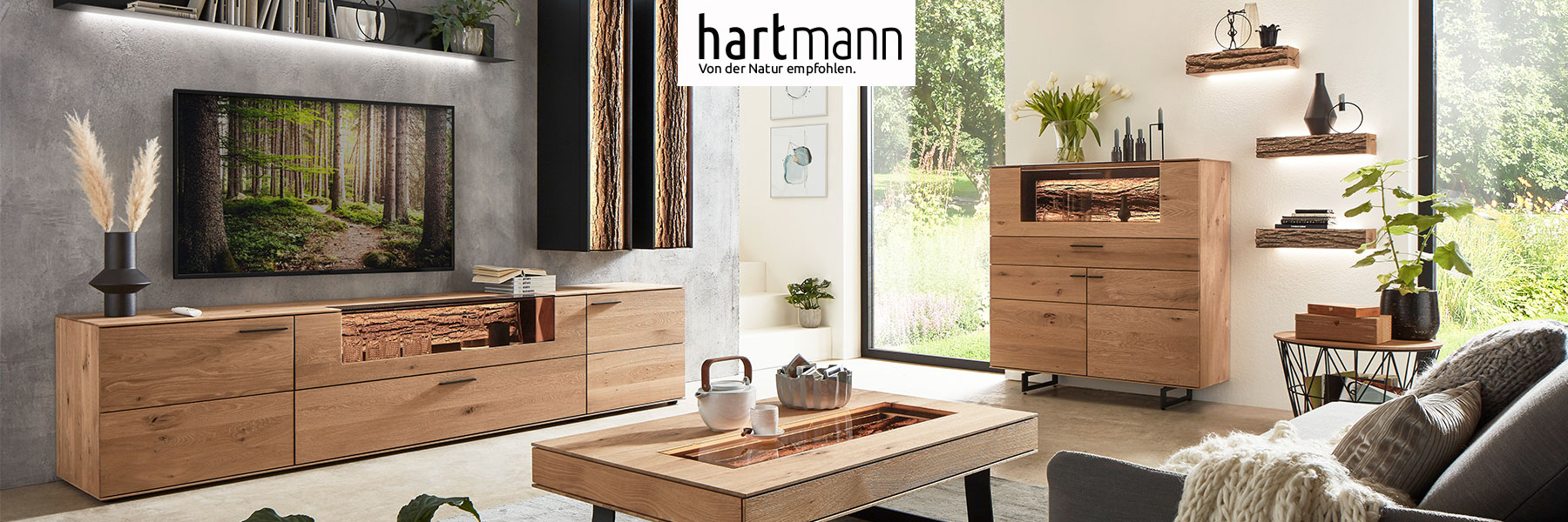 Hartmann Möbel - Möbelserie RUNA - Kerneiche Natur Hartmann RUNA - Massivholzmöbel aus Kerneiche Natur kombiniert mit echter Baumrinde und Metall anthrazit. Ambientebild zeigt Lowboard mit Glasklappe, rechts zwei Hängeschränke mit Rindenfront, an der Wand stehend passendes Highboard und drei Wandregale.