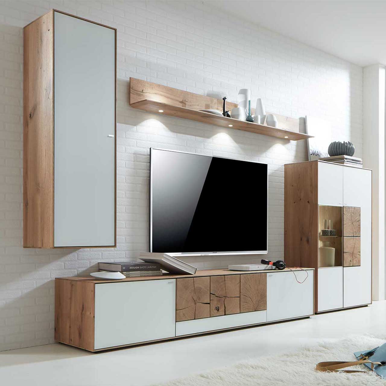 Wohnzimmer mit TV und moderner Massivholz Wohnwand aus Kerneiche Umato mit Mattglas weiß Fronten und rechteckigen Hirnholzscheiben: Hängeschrank, beleuchtetes Wandregal, Lowboard mit Hirnholz, Highboard mit Glasausschnitt und Hirnholz.