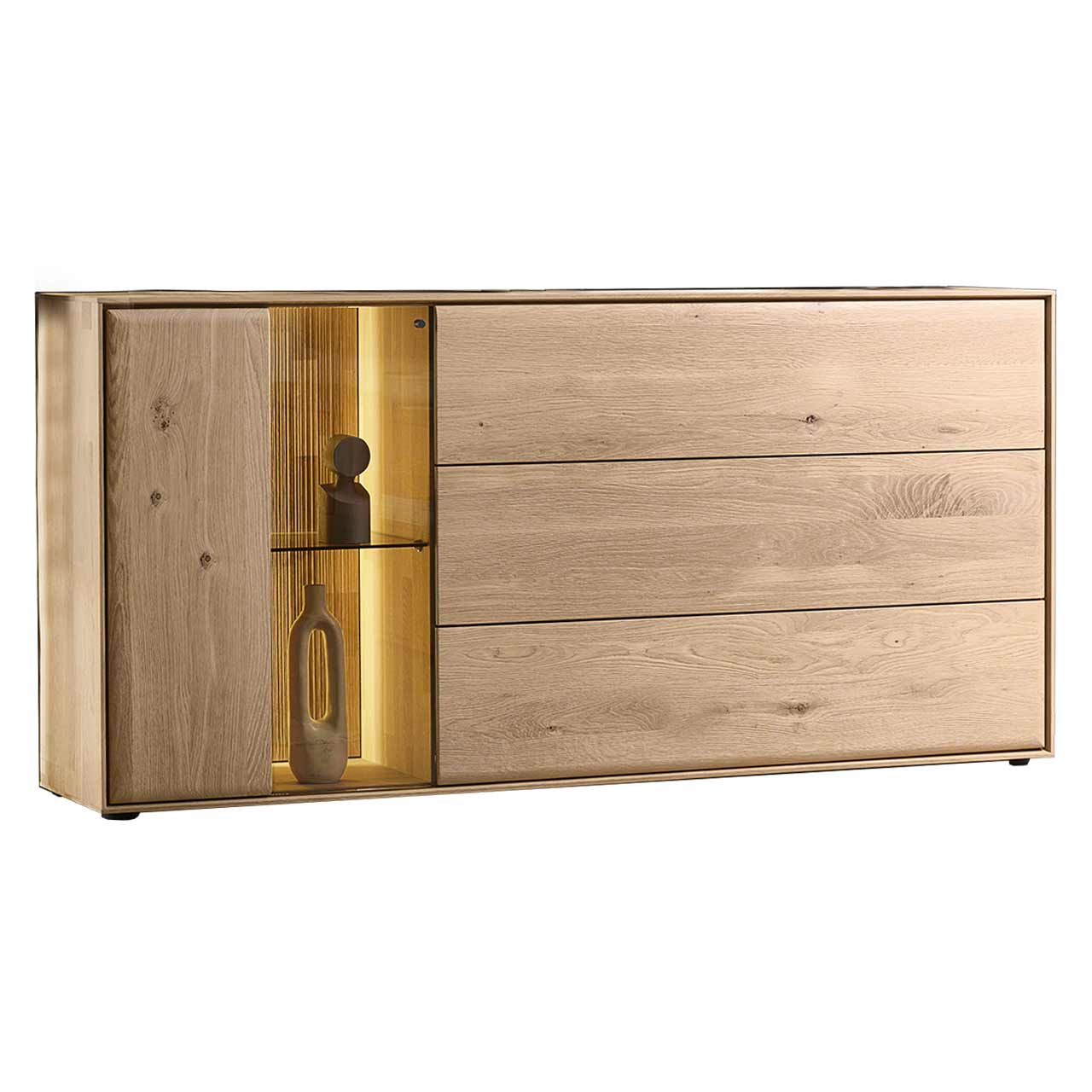 Modernes Sideboard aus massiver Kerneiche Natur mit einer beleuchteten Glas/Holztür links und einer Holzklappe und zwei Holzschubkästen rechts - in Seitenansicht. 