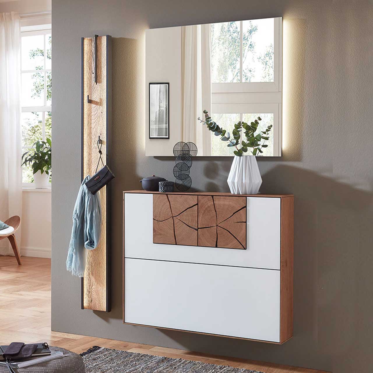 Dreiteilige Garderobe aus massiver Kerneiche mit beleuchtetem Spiegel, einem Schuhkipper mit weißer Mattglasfront und Hirnholzscheiben und einem Garderobenpaneel mit Stange und Haken aus Riffholz und Metall Anthrazit - vor dunkelgrauer Wand .