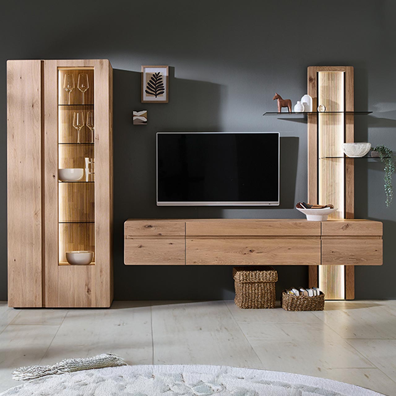 Moderne dreiteilige Wohnwand aus massiver Kerneiche Natur bestehend aus einer Standvitrine mit zwei Türen, einem Hängelowboard und einem integriertem Aufsatzpaneel mit beleuchteten Glasböden und geschroppter Rückwand.