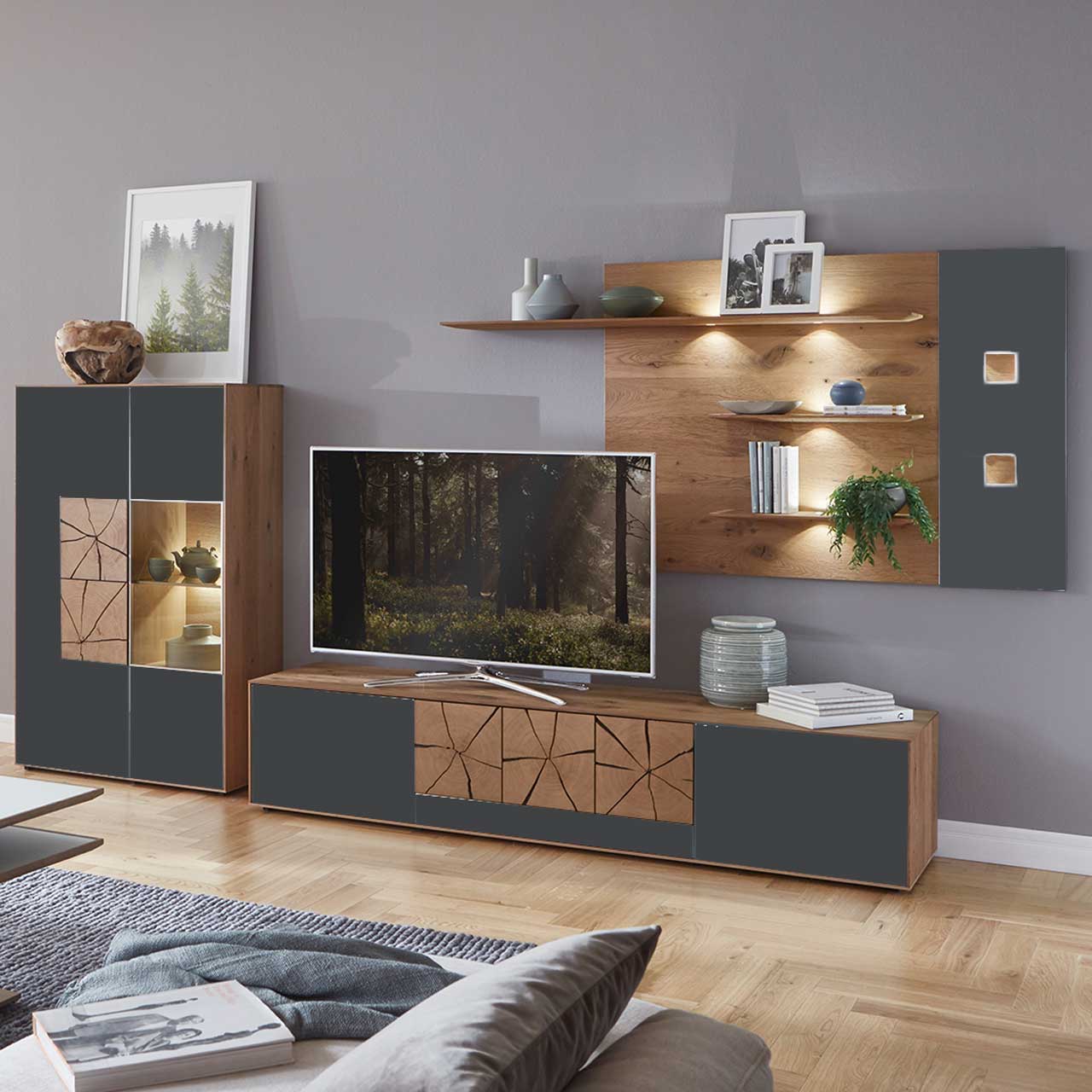 Milieubild Hartmann CAYA - Wohnkombination 7170 Nr. 24A Wohnzimmer mit moderner dreiteiliger Massivholz Wohnwand mit Mattglas Anthrazit Fronten und dekorativen Hirnholzscheiben: Langes Lowboard mit Hirnholz, Wandpaneel mit Regalböden, Highboard mit beleuchtetem Glasausschnitt und Hirnholz.