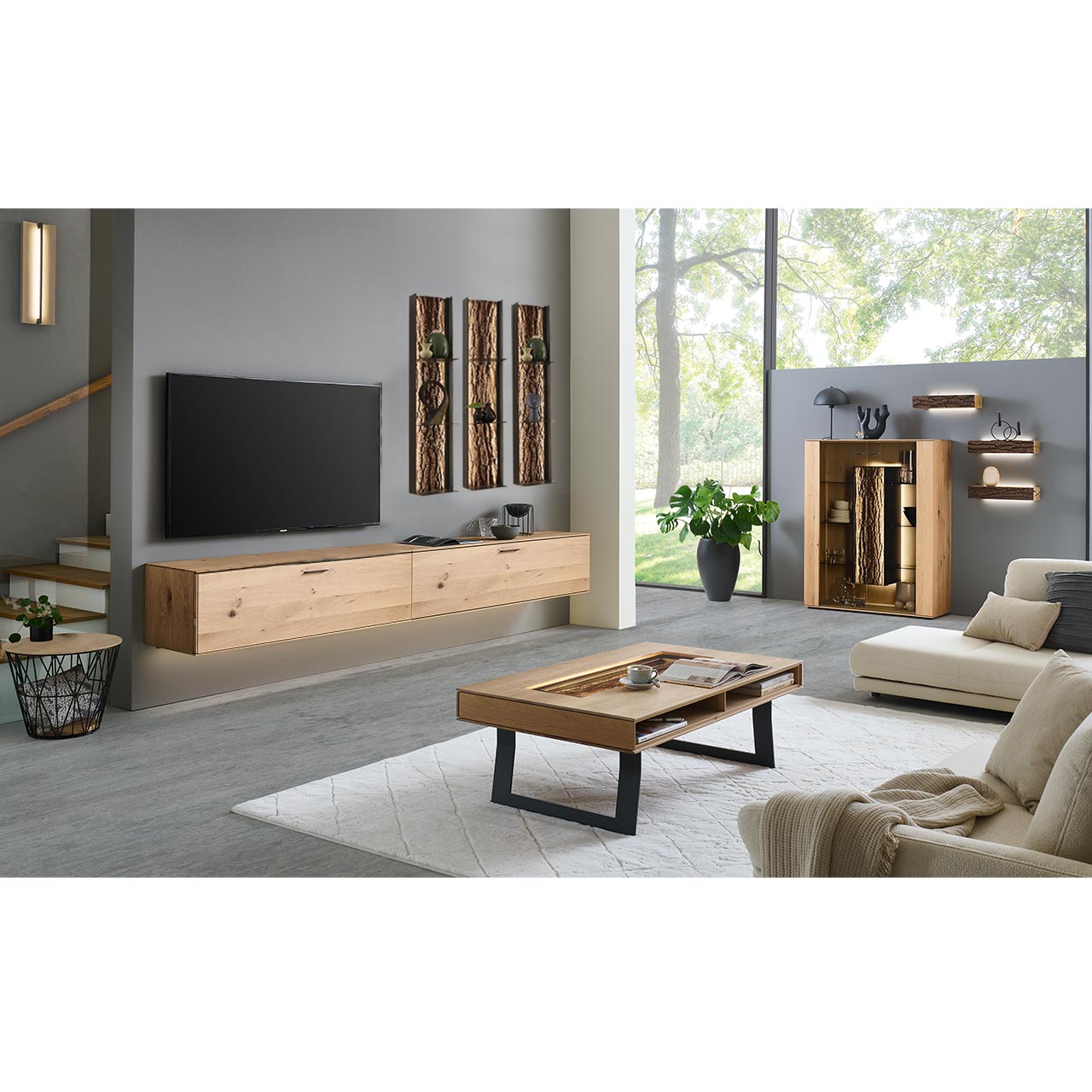 Wohnzimmer mit Wohnwand bestehend aus zwei Hängelowboards aus massiver Kerneiche Natur, und drei beleuchteten Metallregalen mit je drei Ablageböden und sichtbarer Rinden-Rückwand. Rechts passendes Highbord, davor moderner Holz-Couchtisch.