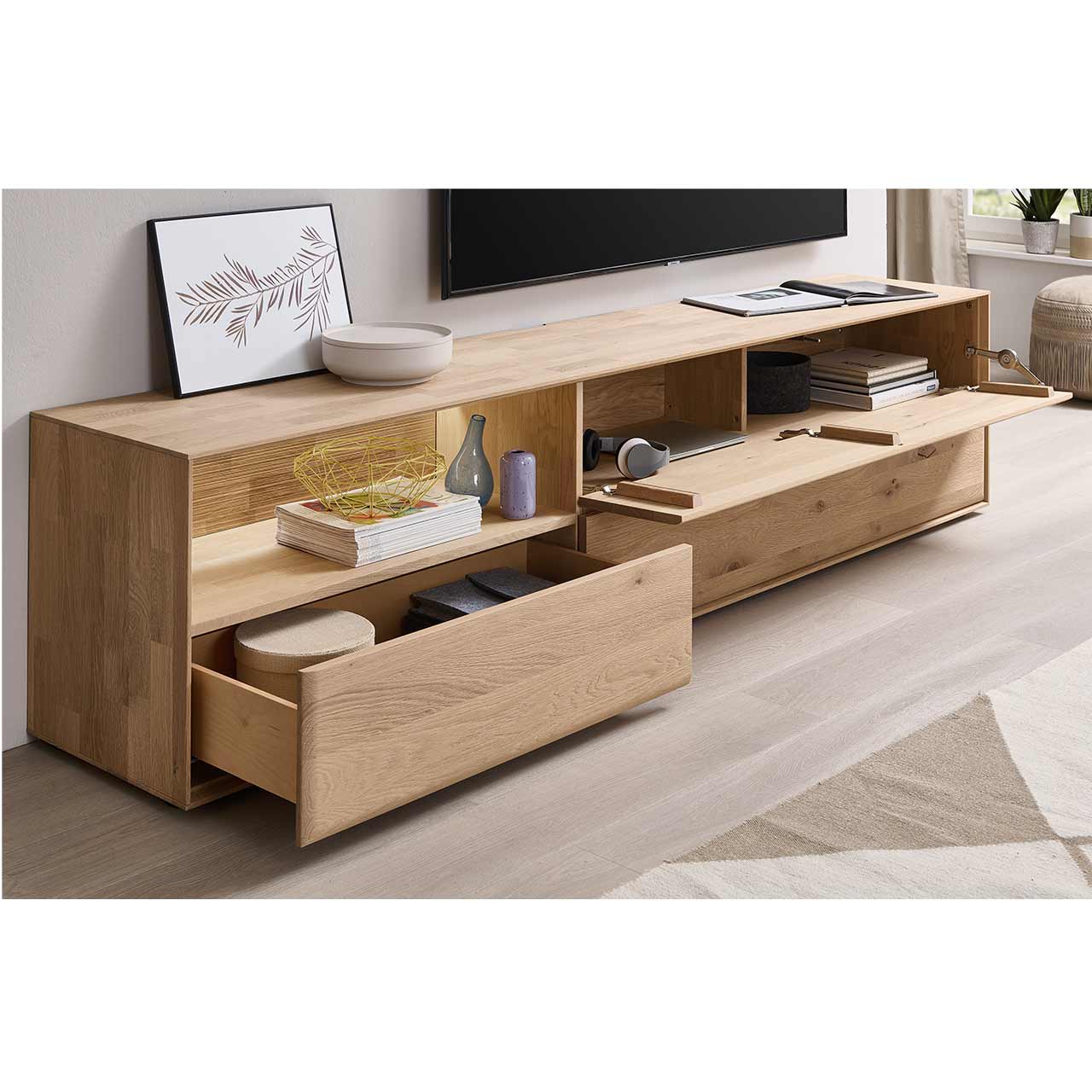 Modernes Lowboard aus massiver Kerneiche Natur mit einem offenem Schubkästen links unten, einer darüber beleuchteten Nische mit geschroppter Rückwand und einer offenen Klappe rechts oben.