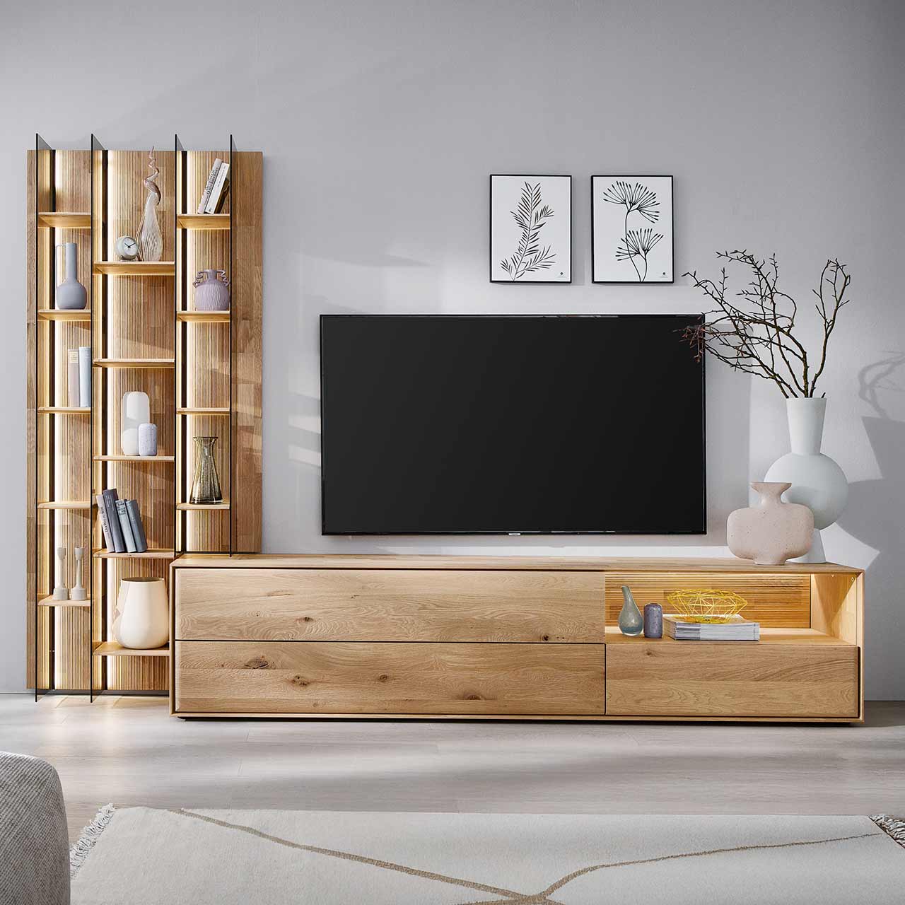 Moderne zweiteilige Wohnwand aus massiver Kerneiche Natur bestehend aus einem hohen Wandregal mit Holzböden, beleuchteten Glasseiten und geschroppter Rückwand und einem darin integriertem Lowboard mit beleuchteter Nische und Schubkasten.