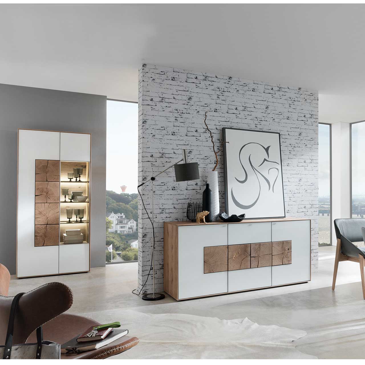 Flur mit modernem Sideboard aus massivem Holz mit Mattglas weiß Front und vier Hirnholzscheiben. Im Hintergrund an einer Wand stehend eine Strandvitrine in Mattglas weiß und beleuchtetem Glasausschnitt mit drei Glasböden.