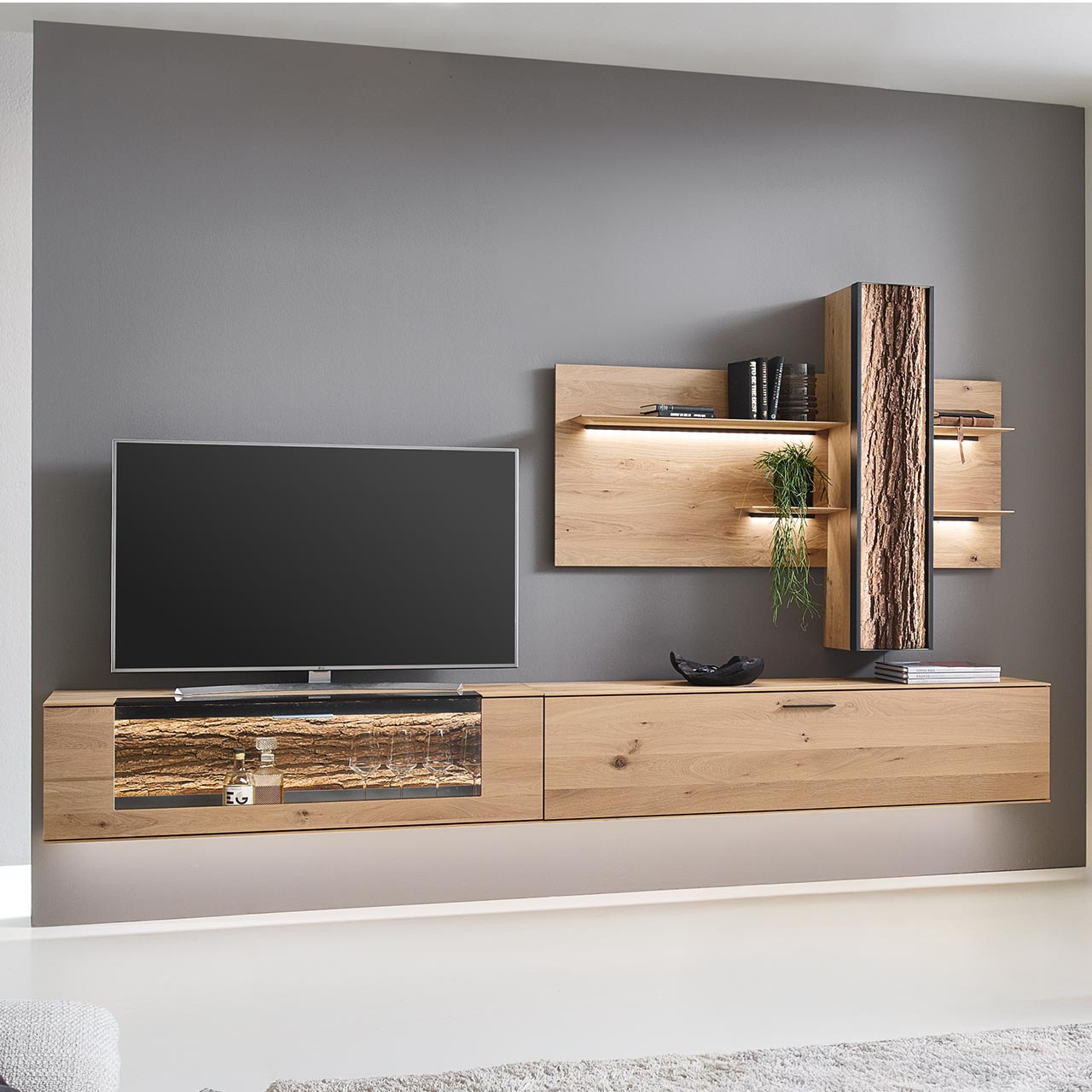 Hartmann RUNA 8410 - Wohnwand Nr. V46 - dreiteilig - Kerneiche Natur und Baumrinde Moderne dreiteilige Wohnwand bestehend aus zwei Hängelowboards aus massiver Kerneiche Natur, eines mit beleuchtetem Glasausschnitt und Rinden-Akzent, und einem Wandpaneel mit vier beleuchteten Holzböden sowie integriertem Stauraumschrank.