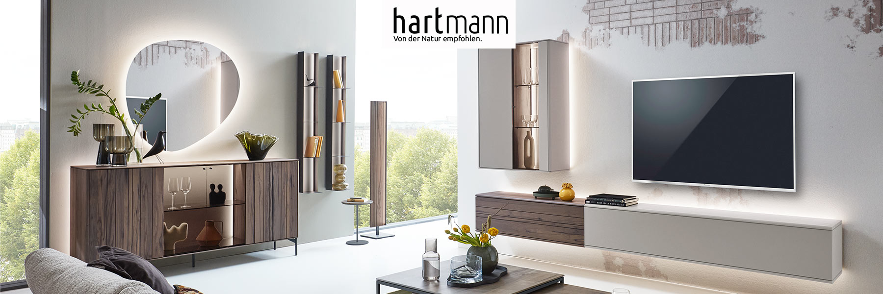 Hartmann Möbel - Möbelserie AUDRA - Altholzbuche Uyaa & Lack sand Hartmann AUDRA - Moderne Möbel aus massiver Altholzbuche Uyaa kombiniert mit sandfarbenen Lackfronten. Ambientebild zeigt Wohnzimmer mit dreiteiliger Wohnwand, Couchtisch, zwei Hängeregale und Sideboard mit Metallfüßen darüber moderner Spiegel.