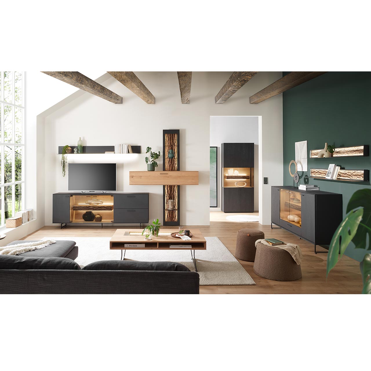 Modernes Wohnzimmer mit Wohnwand, Sideboard, Vitrine und Wandregalen aus massiver Kerneiche Natur anthrazit gebeizt, teils mit beleuchteten Glasausschnitten und Rinden-Akzenten. Im Vordergrund ein passender Couchtisch.