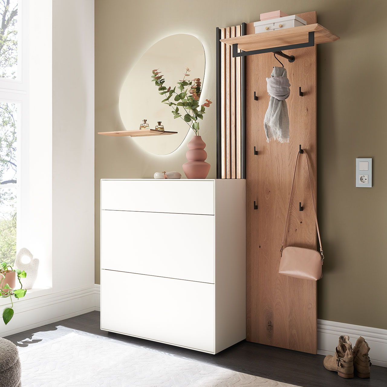 Moderne dreiteilige Garderobe aus Kernbirke und Kerneiche Natur: Wandpaneel aus Holz mit Kleiderstange, Haken und Lamellen-Akzent, ein Stauraumschrank mit Schubkasten und Klappen in Lack weiß und ein ovaler Spiegel mit Ablage.