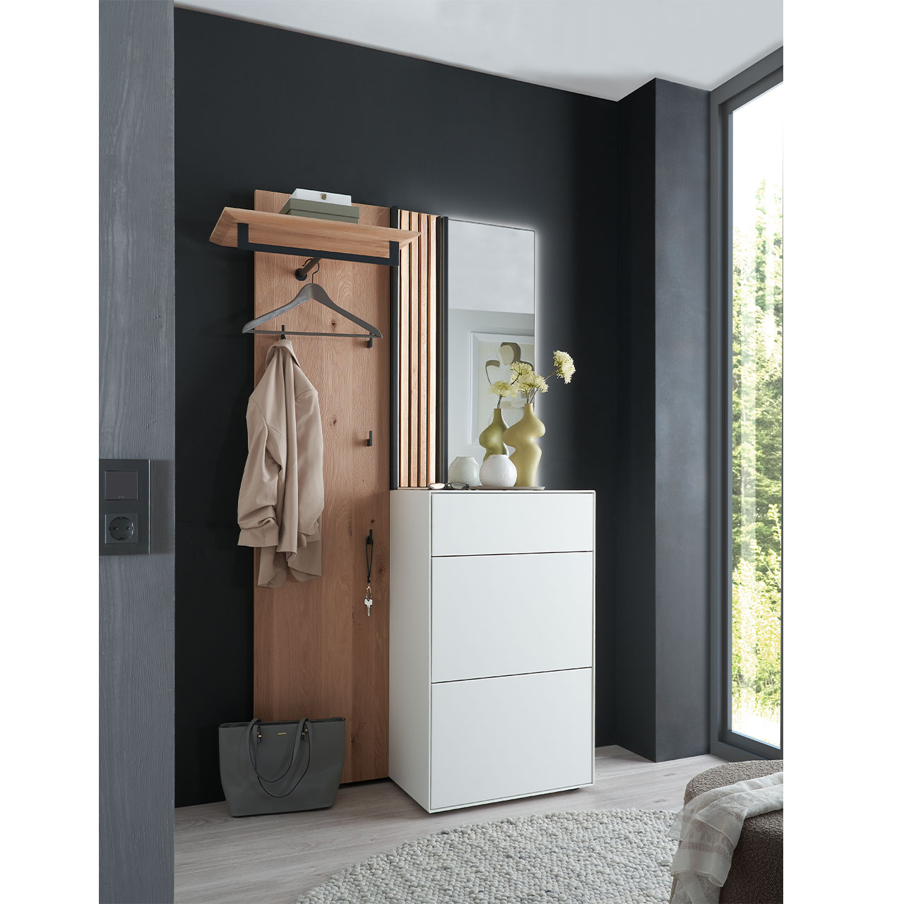 Flur mit modernen Garderobenmöbeln aus Kernbirke und Kerneiche Natur: Wandpaneel aus Holz mit Kleiderstange, Haken und Lamellen-Akzent, ein Stauraumschrank mit Schubkasten und Klappen in Lack weiß, ein rechteckiger Spiegel.
