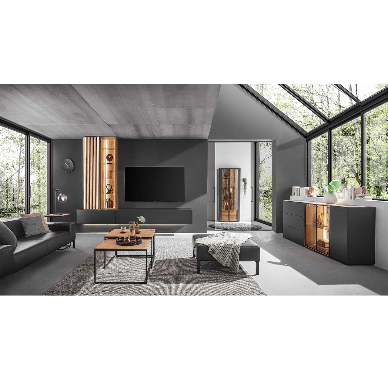 Modern eingerichtetes Wohnzimmer mit vierteiliger Wohnwand in Anthrazit kombiniert mit hellem Holz und Lamellen. Mit passendem Sideboard rechts und minimalistischem Couchtisch im Vordergrund.