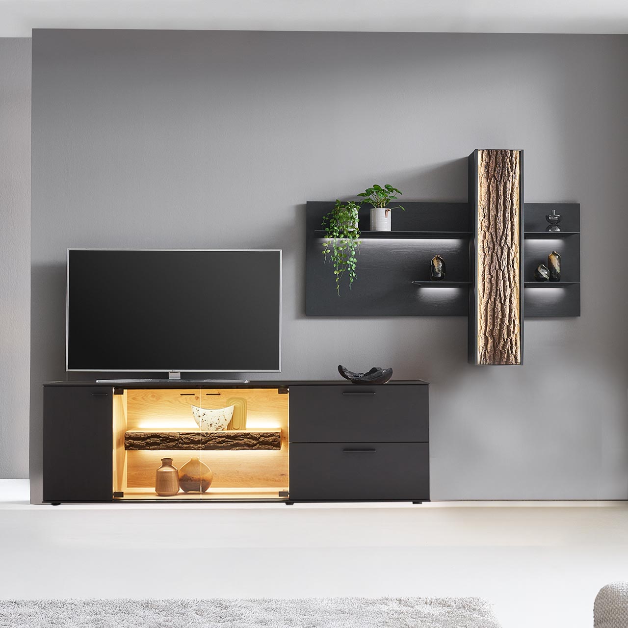Moderne zweiteilige Wohnwand bestehend aus einem Lowboard in Kerneiche Natur anthrazit gebeizt mit Glasausschnitt und Rinden-Akzent und passendem Wandpaneel mit beleuchteten Böden und integriertem Stauraumschrank mit Rinden-Front.