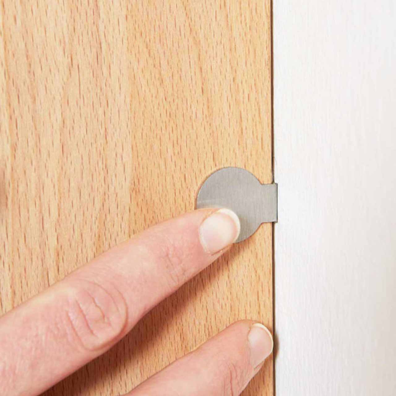 Bildausschnitt eines runden, silbernen Touchschalters angebracht an einem Holzmöbelstück, der per Zeigefinger betätigt wird.